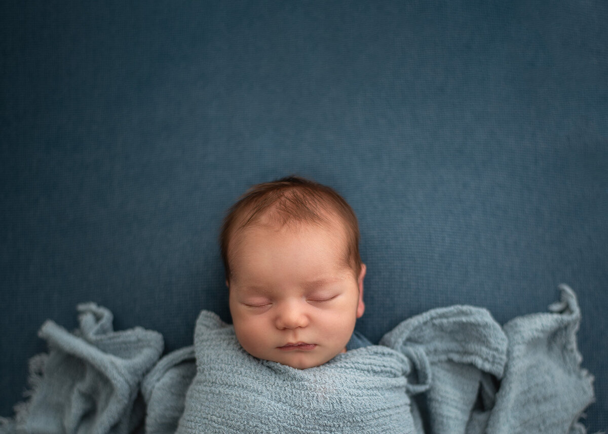 newborn on blue and tucked in at newborn photo session