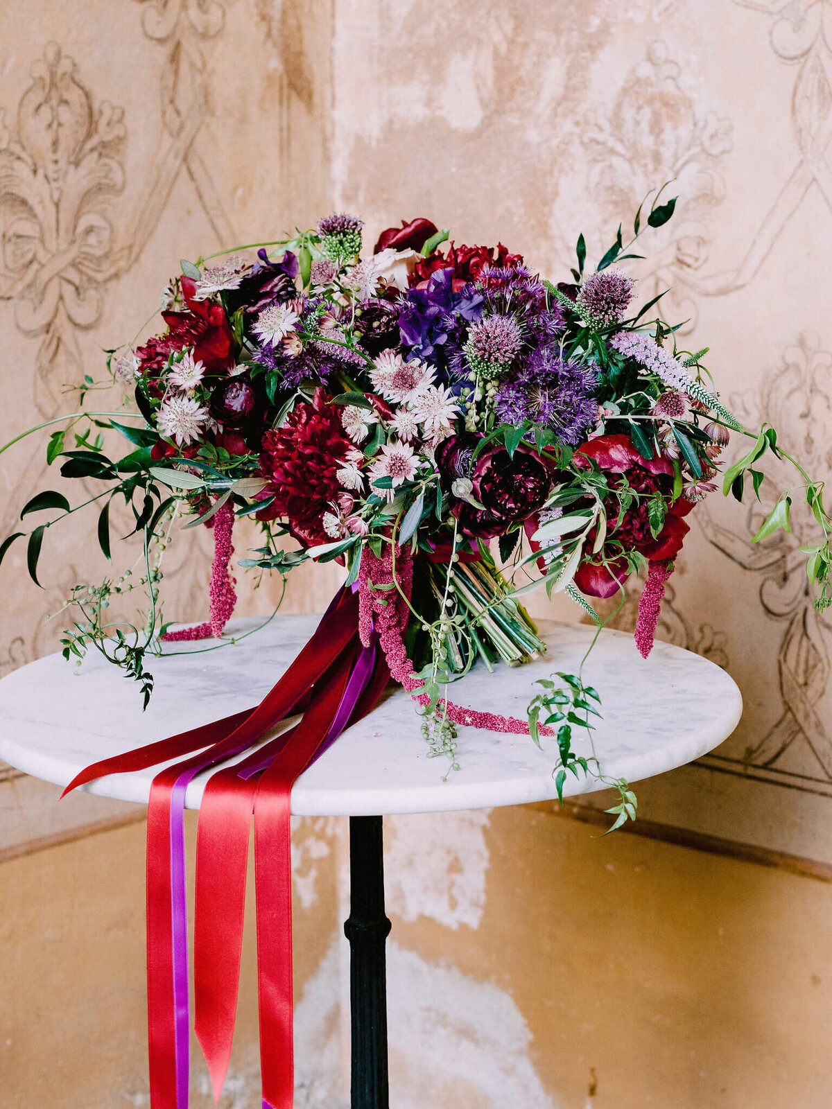 Big flower bouquet of red, blue, white, pink and purple colors on a table, with red and purple laces flowing down the table