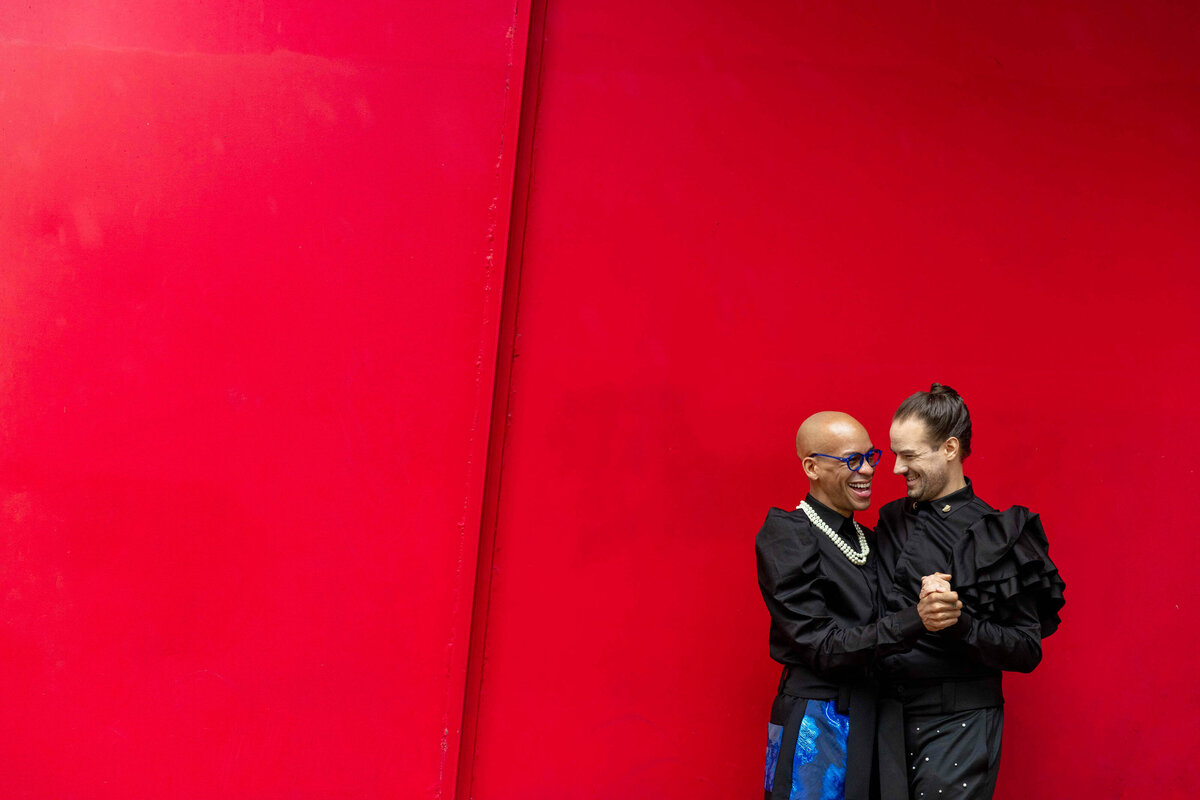 Two people standing next to each other in front of a red wall.