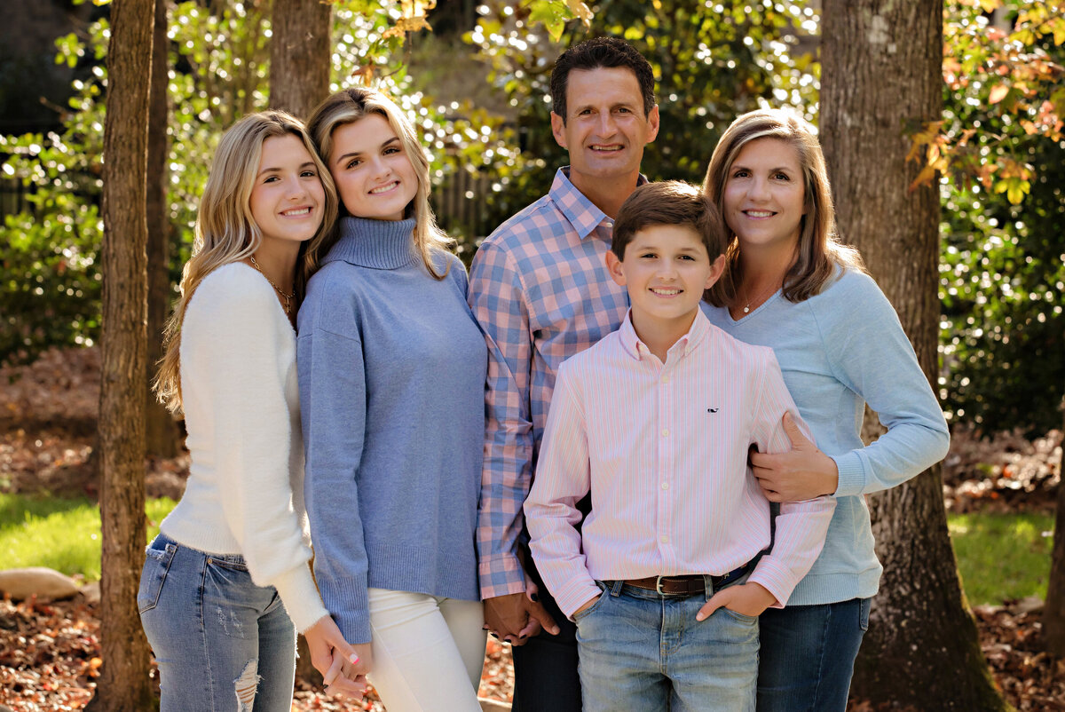 Sweet family of 5 including two teenage daughters and a middle school age son along with Mom and Dad in a blue, light blue and pink color scheme with jeans for a perfect casual family portrait.