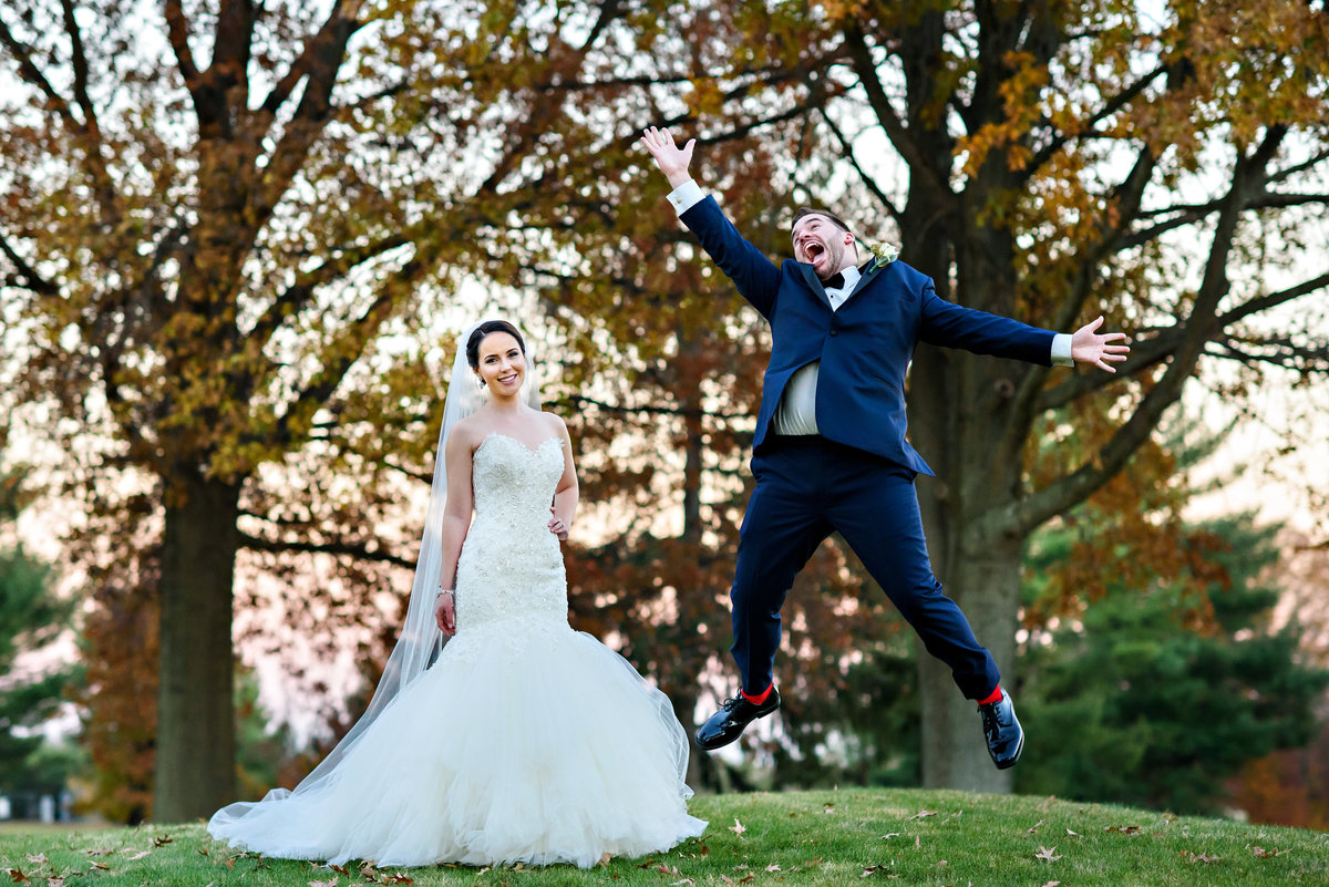 A groom jumps for joy while his bride laughs with excitement at their Northampton Valley Country Club Wedding.