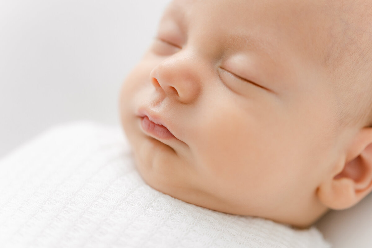 A closeup photo of a baby's face in a white swaddle by Washington DC Family Photographer