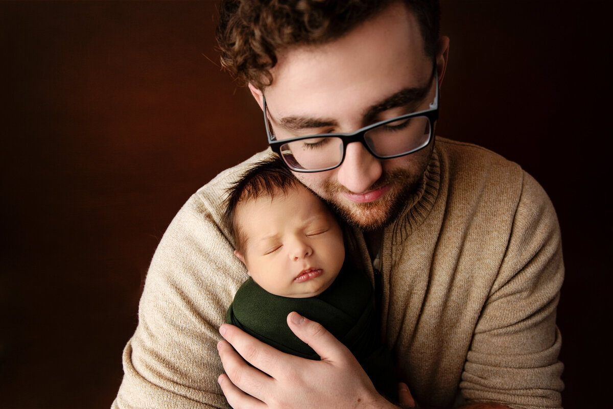 st-louis-newborn-photographer-dad-holding-newborn-baby-boy-on-brown-backdrop