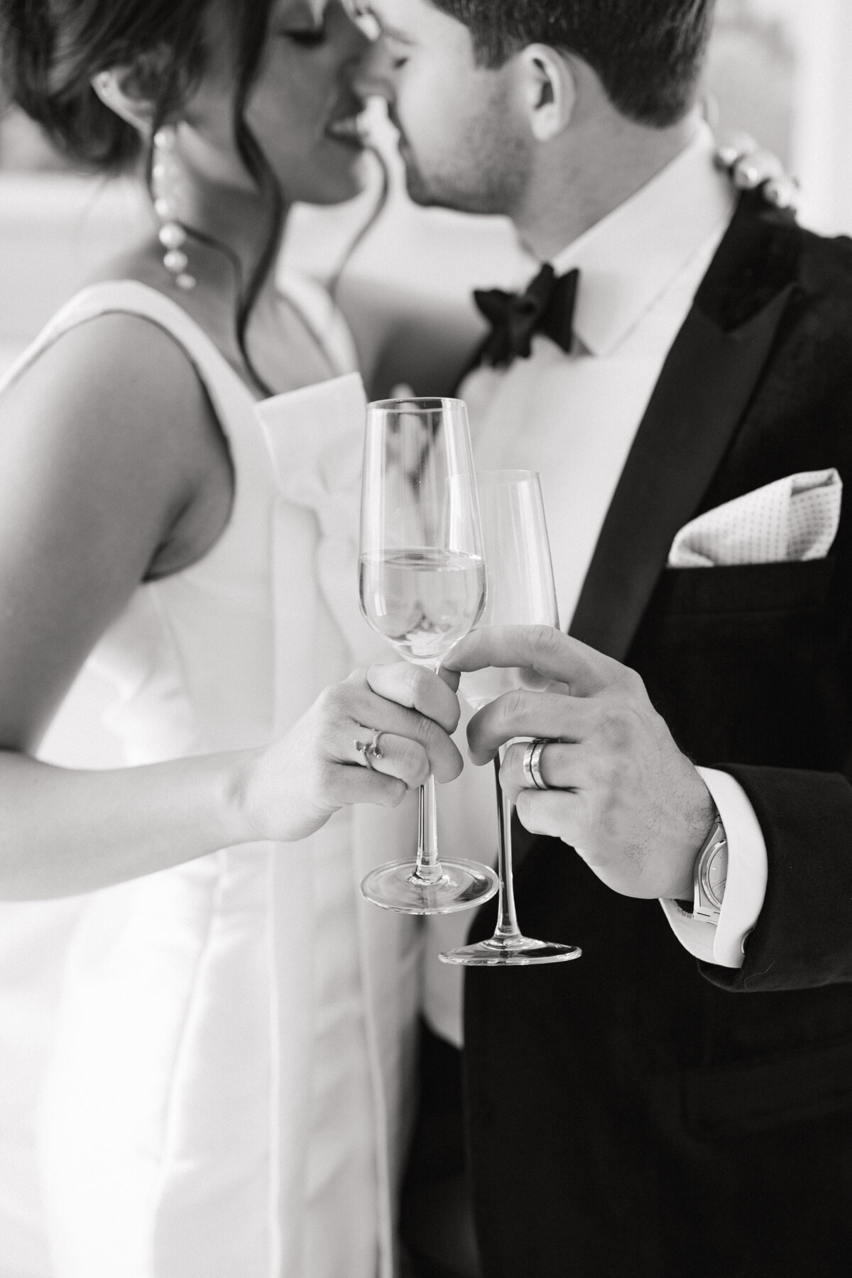 black and white image of bride and groom cheersing their champagne glasses about to kiss.