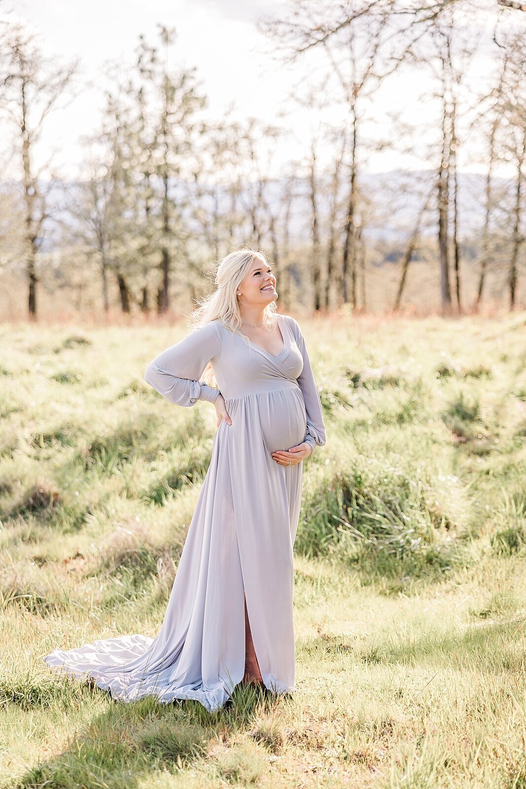 solo maternity portrait of expecting woman smiling and looking up on warm  sunny day