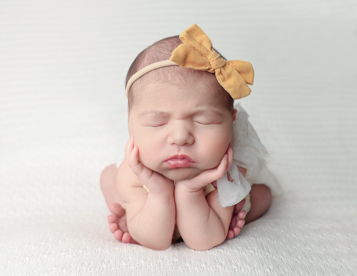 Newborn girl peacefully posed in frog position amidst a soft backdrop at a photography studio in Rochester, NY, showcasing her innocence and delicate features.