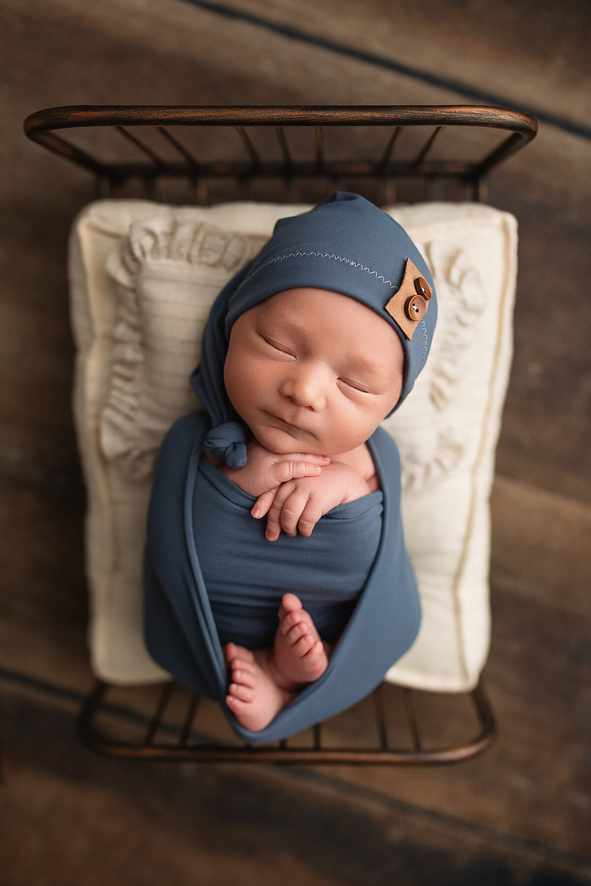 Newborn baby boy wrapped in a slate blue wrap with matching sleepy cap.