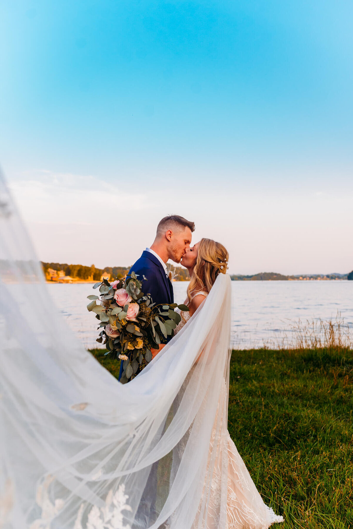 Photo of a bride and then kissing while the veil flows in front of them and a river is in the background