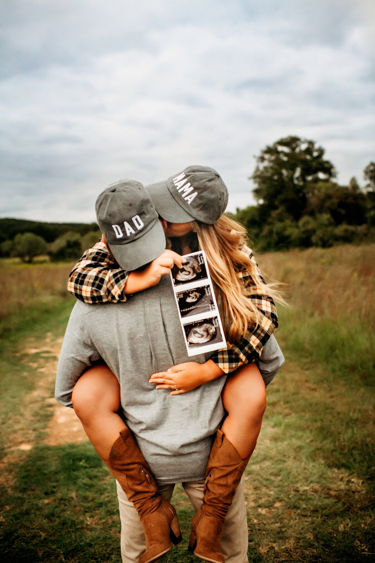 Couples Photography, Man with a hat that says "Dad" is holding a woman wearing a hat that says "Mama" as she holds an ultrasound picture.