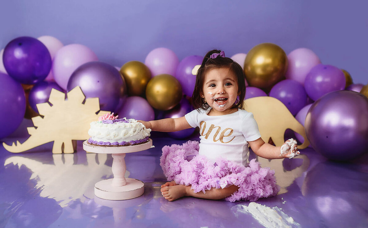 Baby smiles at the camera during her first birthday cake smash photoshoot at Asheville Photo Studio.