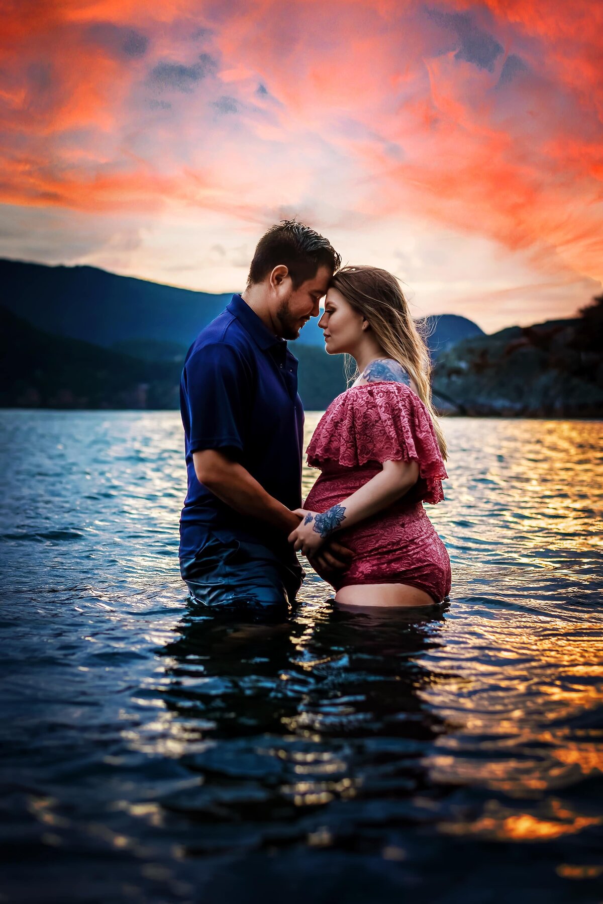 Pregnant woman and husband in the ocean at sunset.