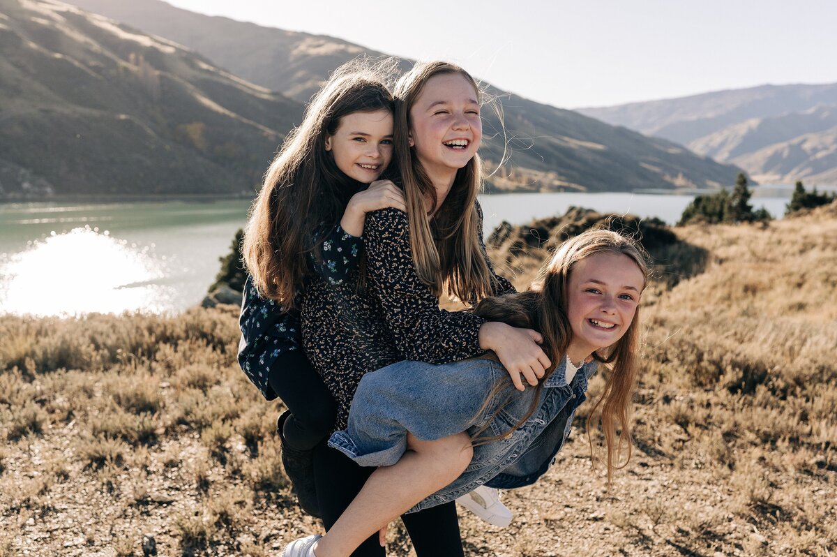 three girls doing candid piggyback for family photo shoot in clyde dunstan lake