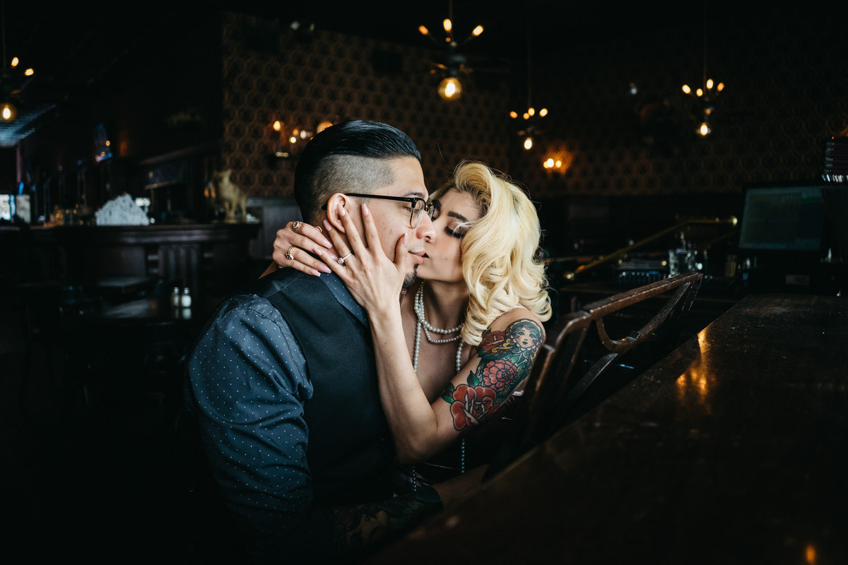Blonde woman kissing her fiancé while he plays the piano.