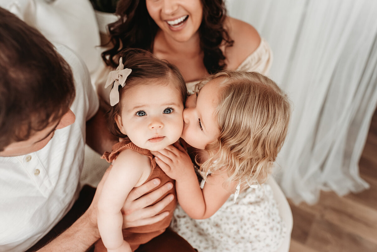 big sister kissing her little sister at her milestone photo session