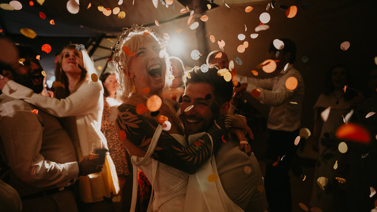 Boho bride is lifted on the dance floor by her groom as confetti falls on their during the end of their first dance. 