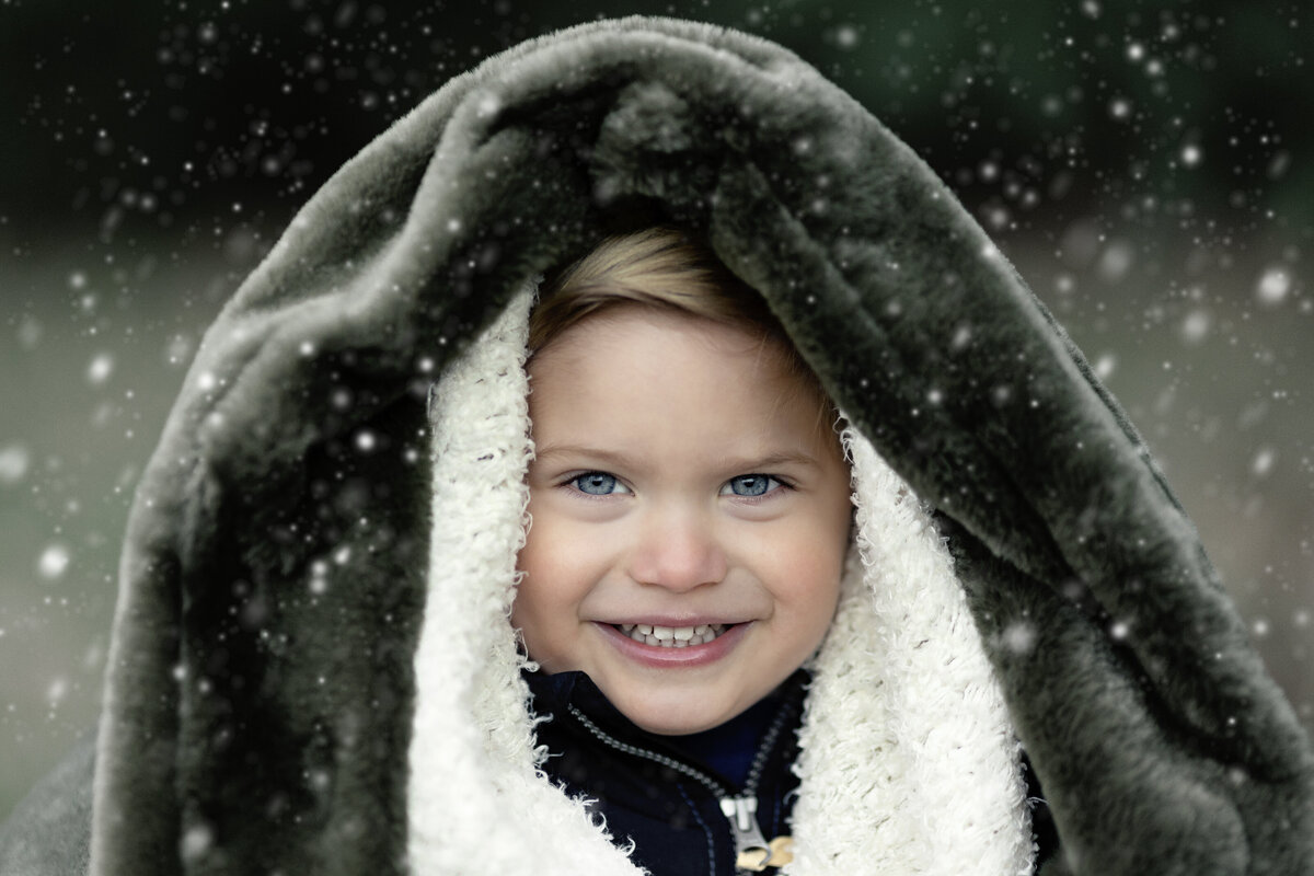 A young child bundles up in a blanket under falling snow