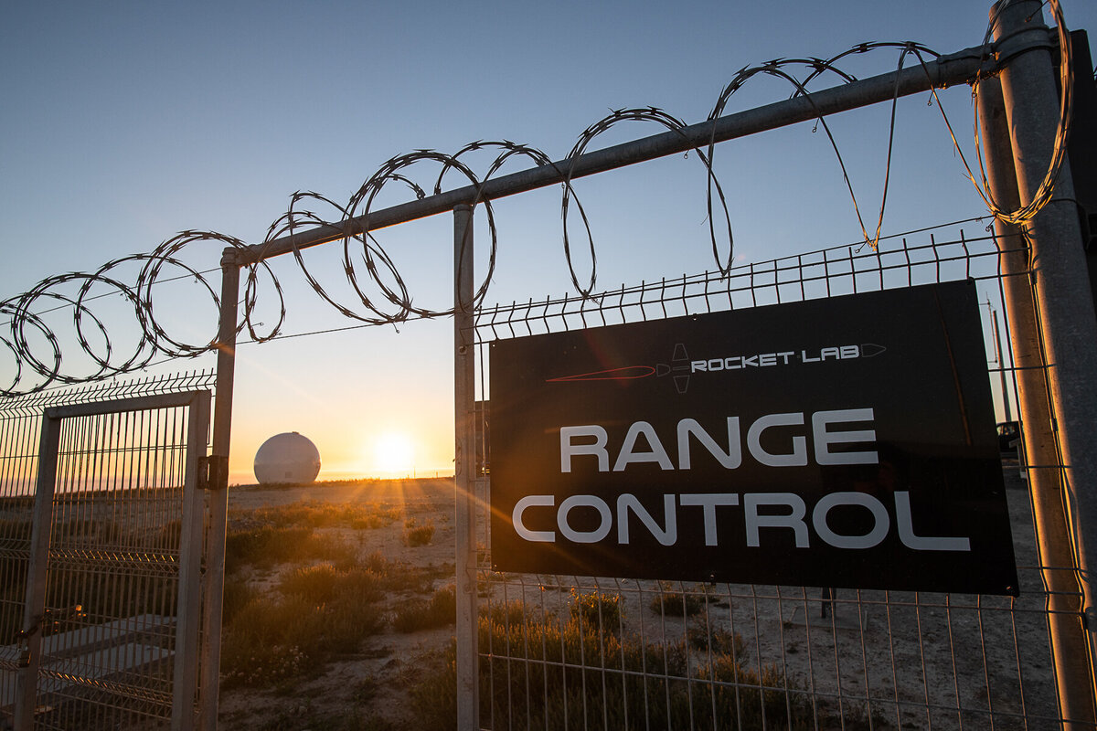 Sunset behind range control  at Rocketlab's Launch Complex 1. Sign detail with radar dome and sun flare behind barbed wire fence.