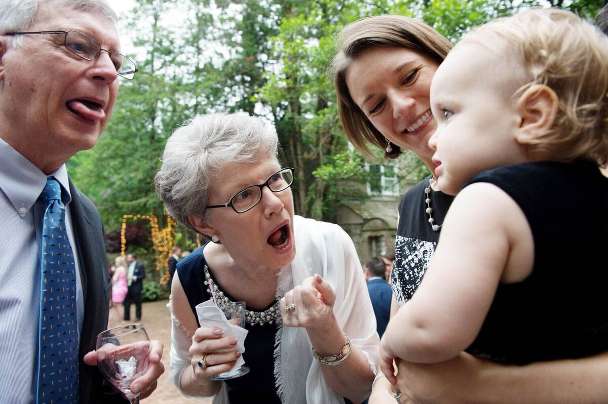 two grandparents make funny faces and stick tongues out at a baby