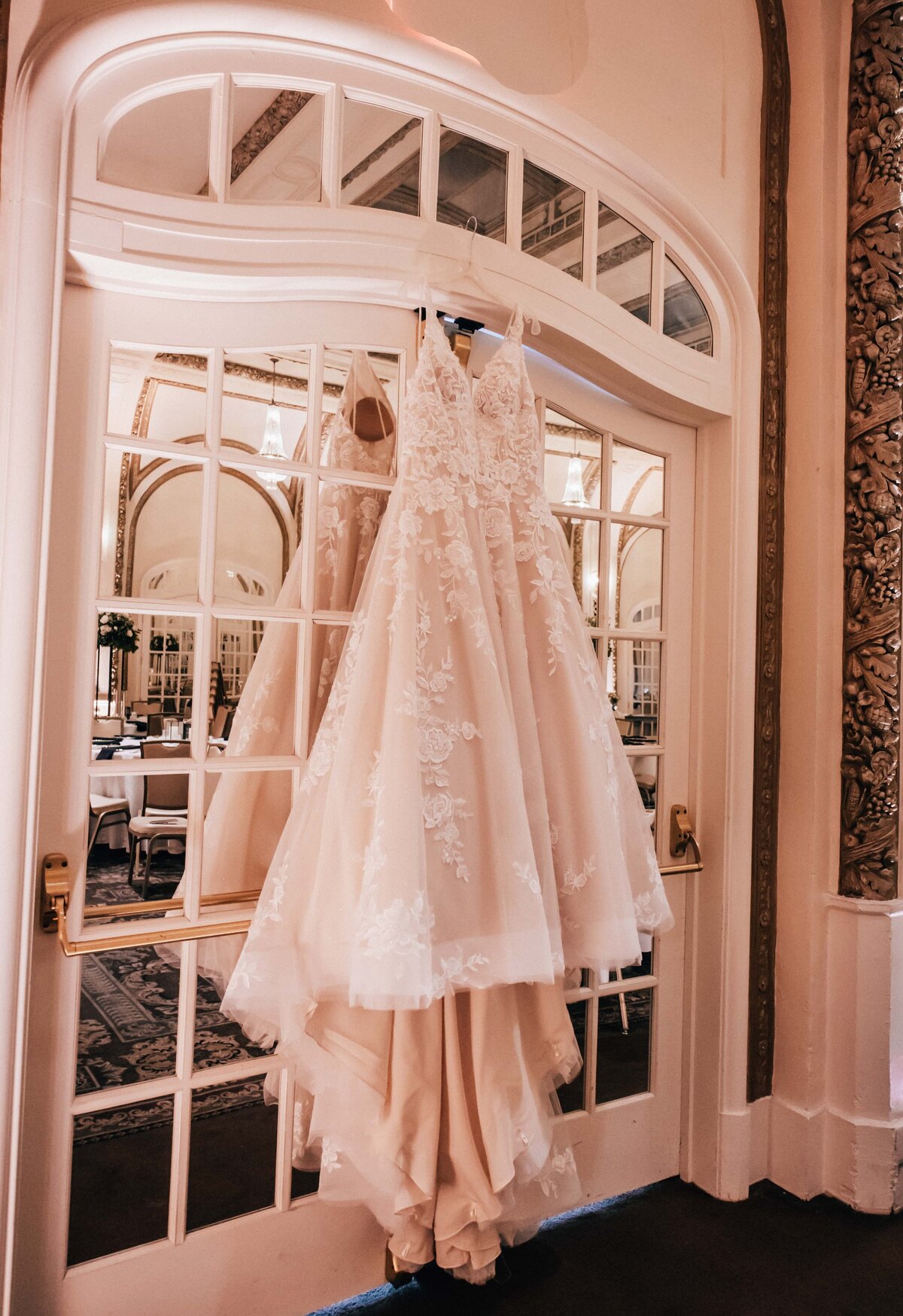An elegant white wedding dress hanging on an arched doorway in a room with vintage decor at a park farm winery wedding.