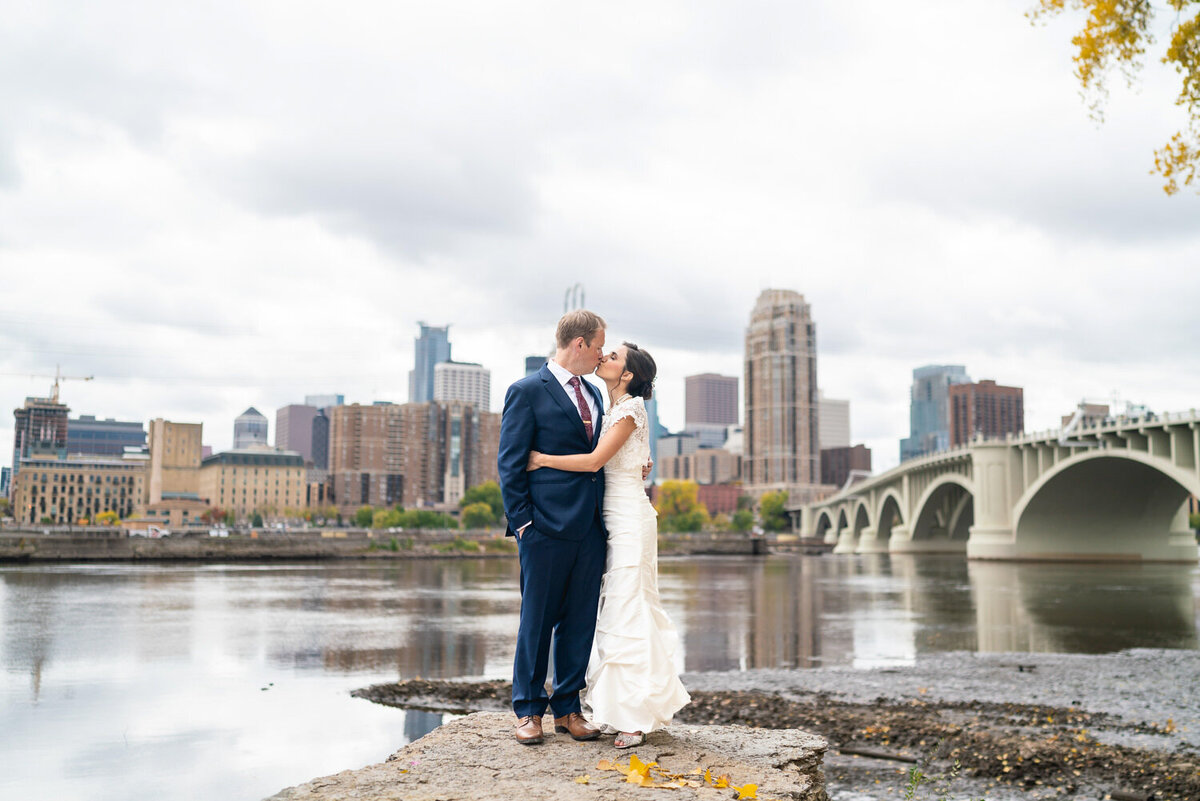 Bride and groom kiss in front of Minneapolis skyline.