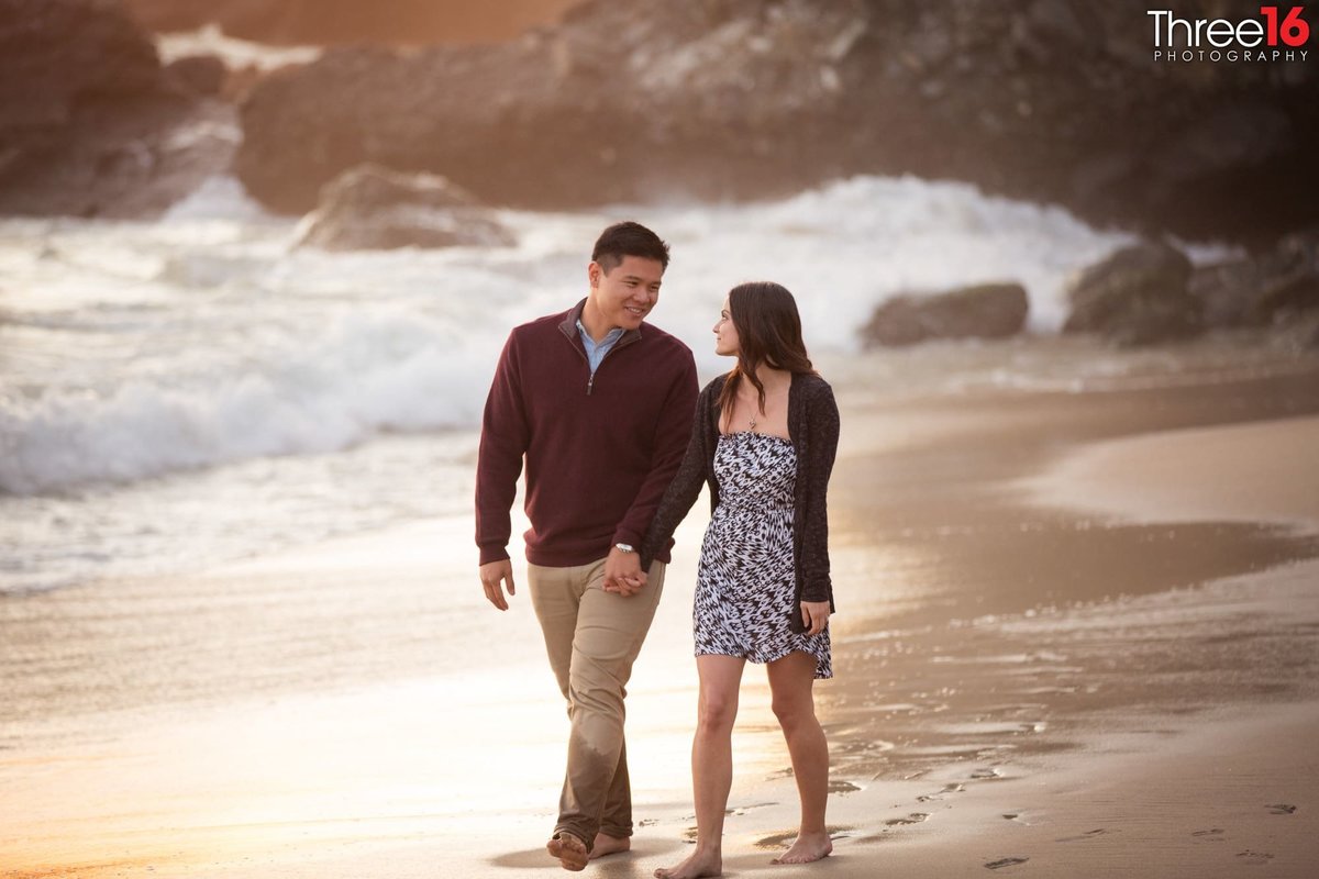 Engaged couple walk hand in hand along Thousand Steps Beach shoreline