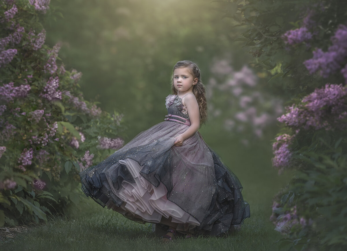 A young girl stands between two rows of lilac bushes twirling her dress. Photo taken in Ottawa.