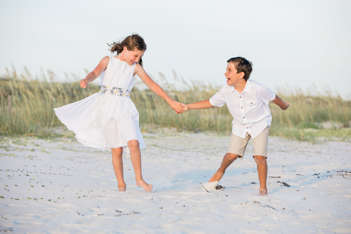 Two kids holding hands and running in the sand