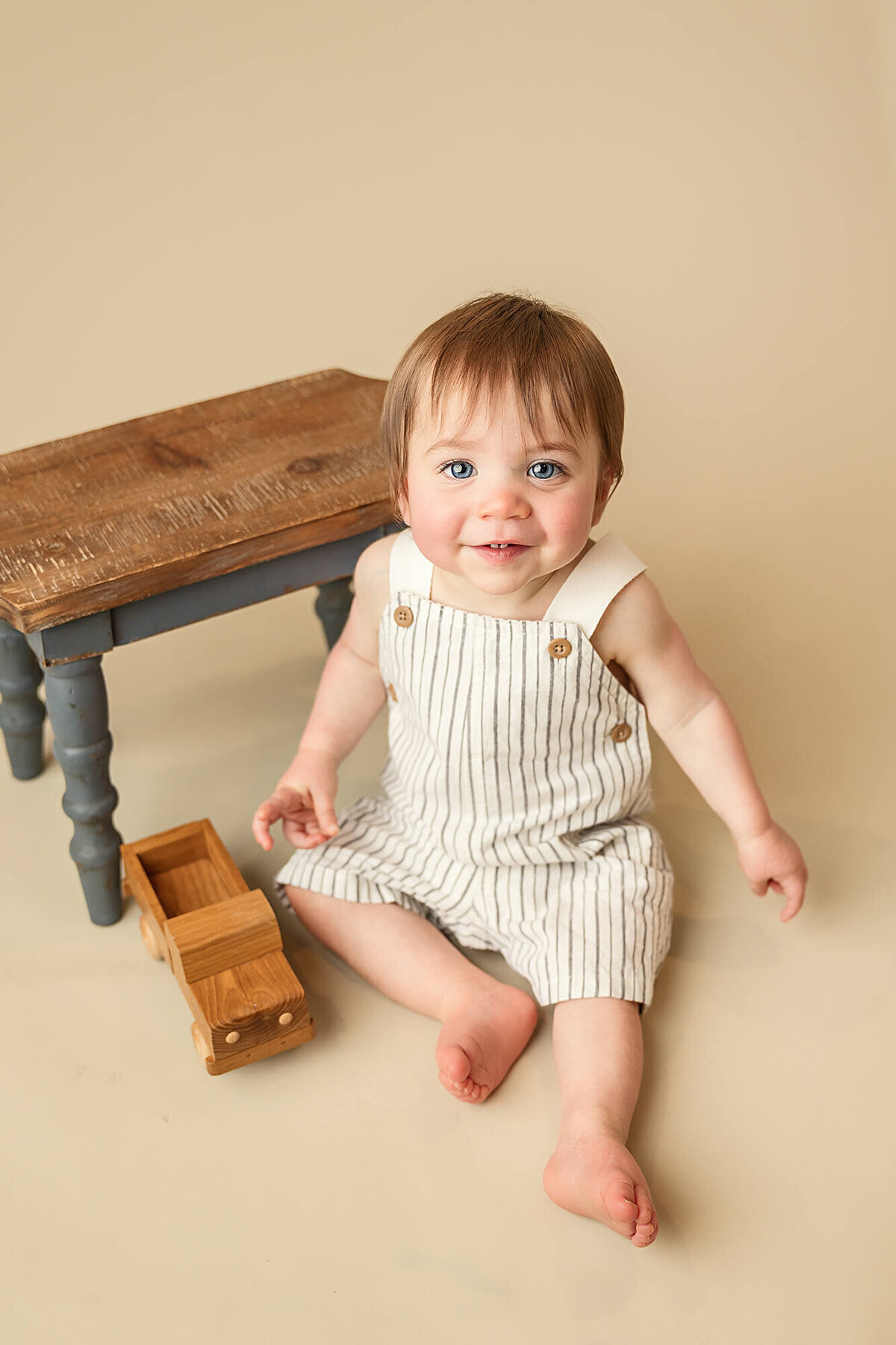 Baby boy wearing a neutral romper poses and smiles for his one year milestone session.