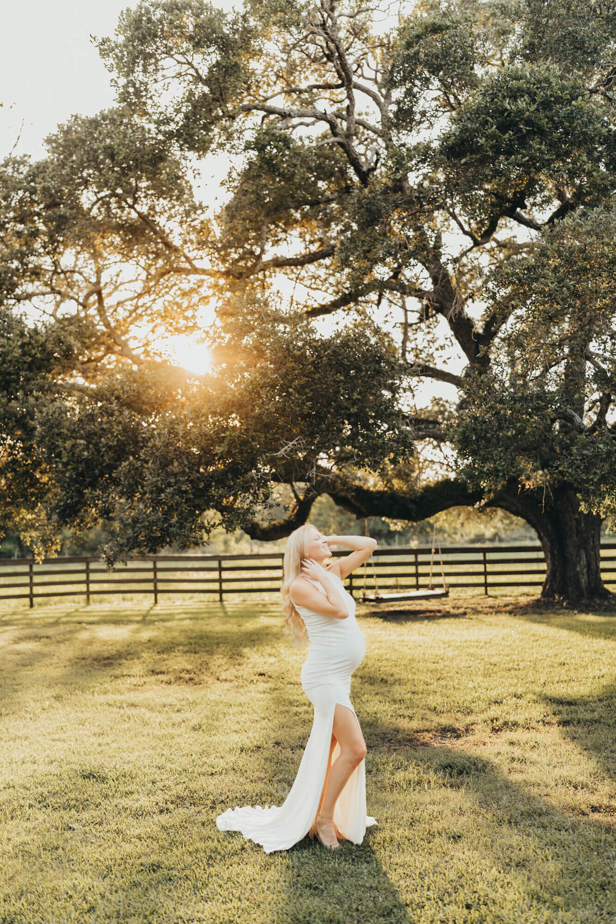 kaylyn wears a fitted white gown for her maternity session in lake jackson under a huge oak tree.