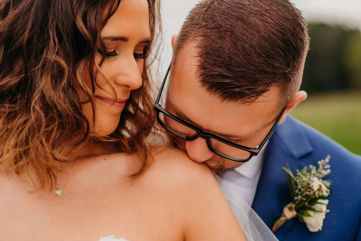 Photo of a groom kissing his bride shoulder while she smiles at him