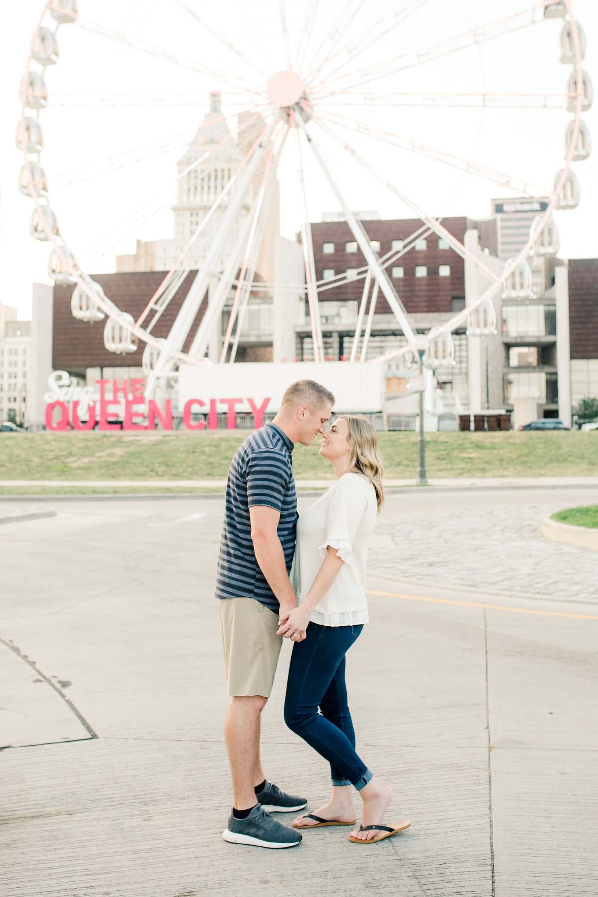 An engaged couple holds hands and faces one another in front of a ferris wheel in Cincinnati Ohio