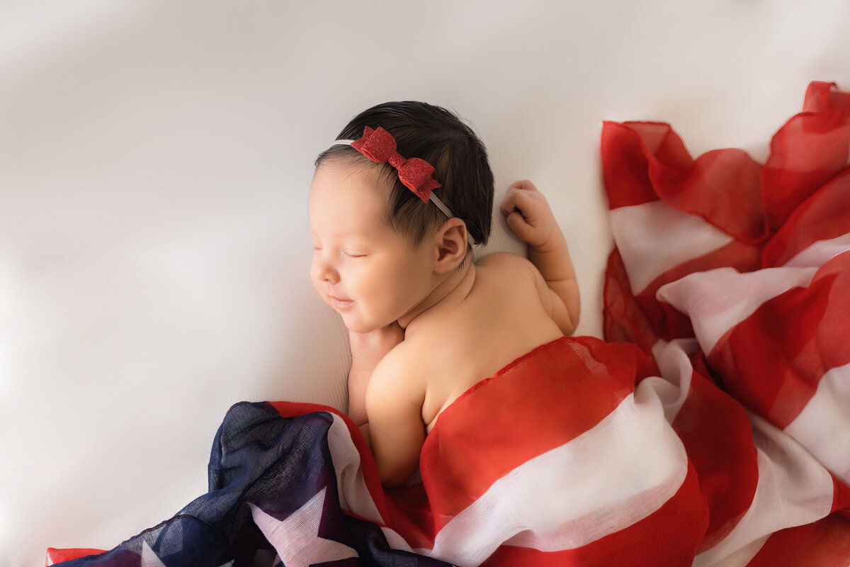 Newborn Photographer, a baby girls sleeps smiling covered in an American Flag blanket
