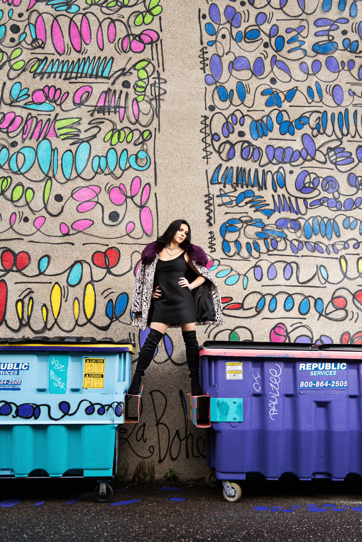 high school senior girl in little black dress and tall boots standing on dumpster