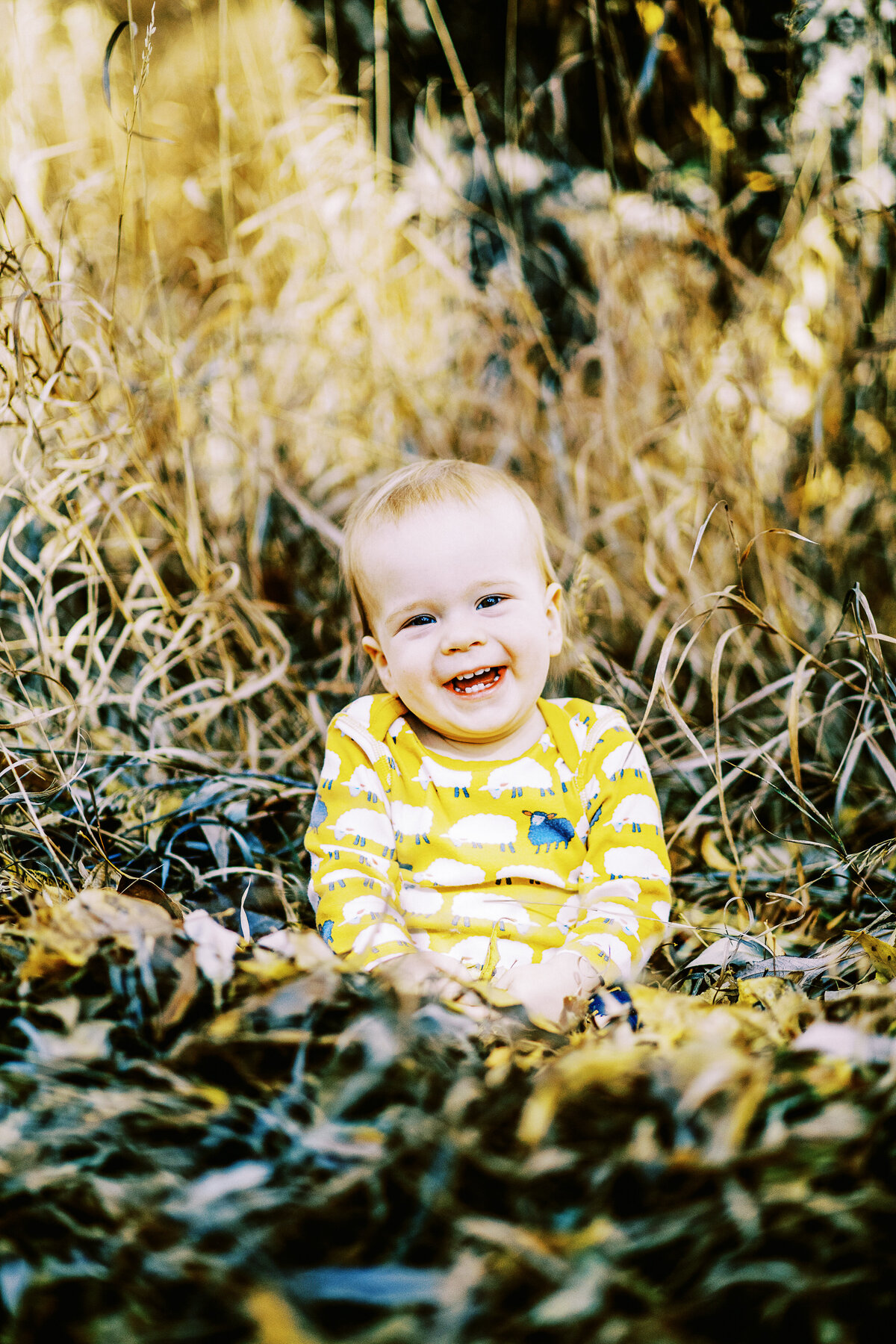a smiling baby boy sits in fall leaves and looks at camera