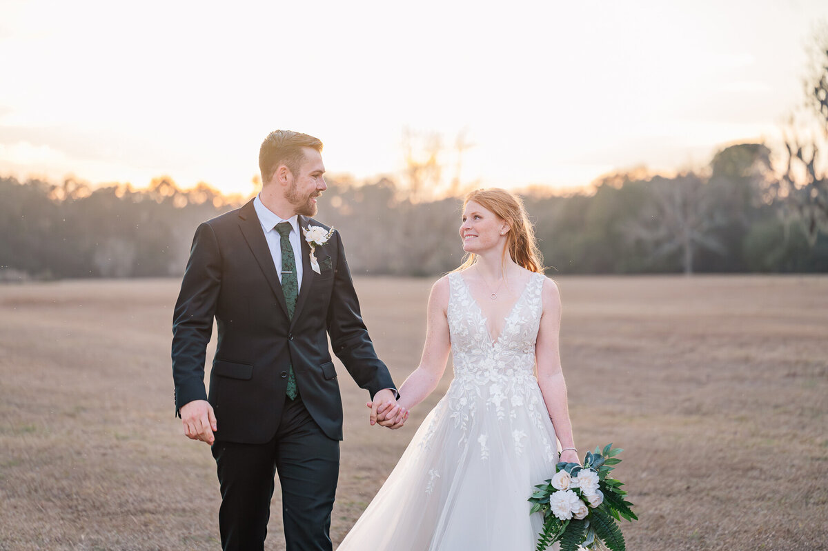 A beautiful newly wed couple walking and holding hands at sunset by JoLynn Photography, a North Carolina wedding photographer