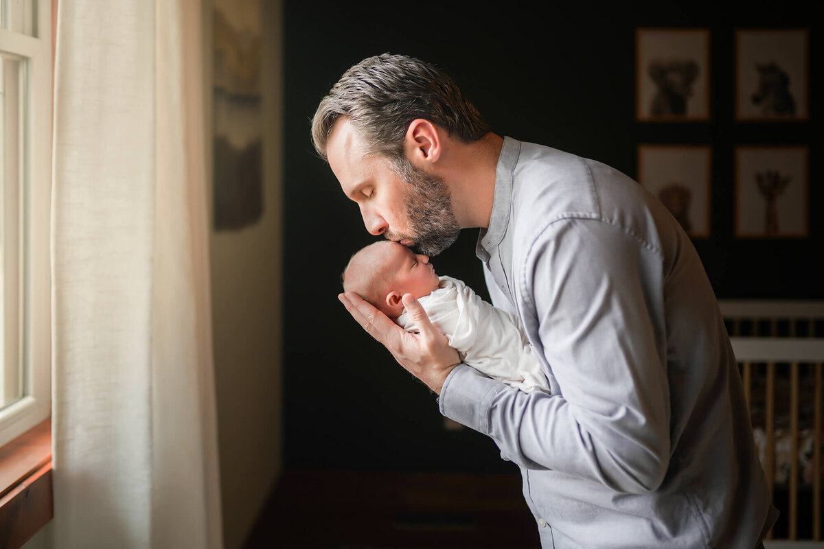A dad holds his newborn baby girl and kisses her forehead