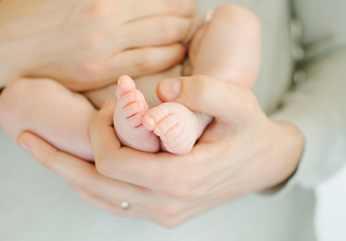 Parent's hand, holding a newborn's feet, captured by Tevi Hardy, Bay area newborn photographer.