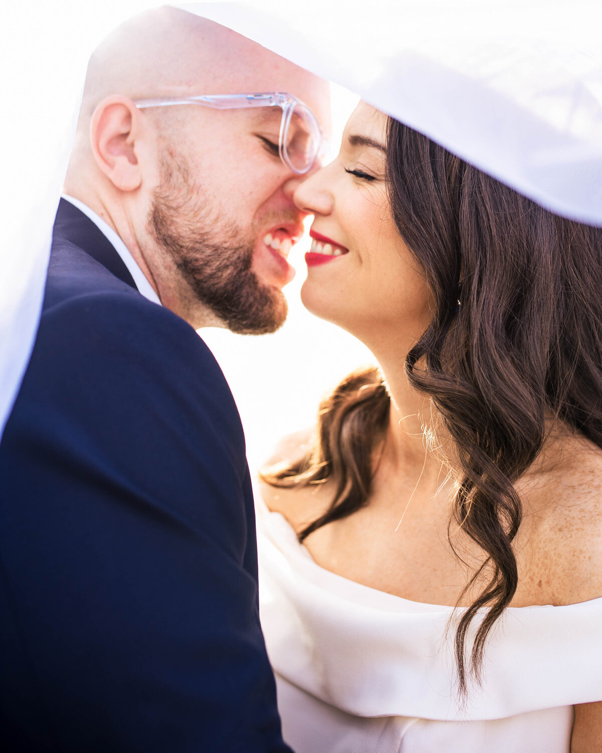 Upclose-photograph-of-bride-and-groom-smiling-just-before-a-kiss-underneath-her-veil