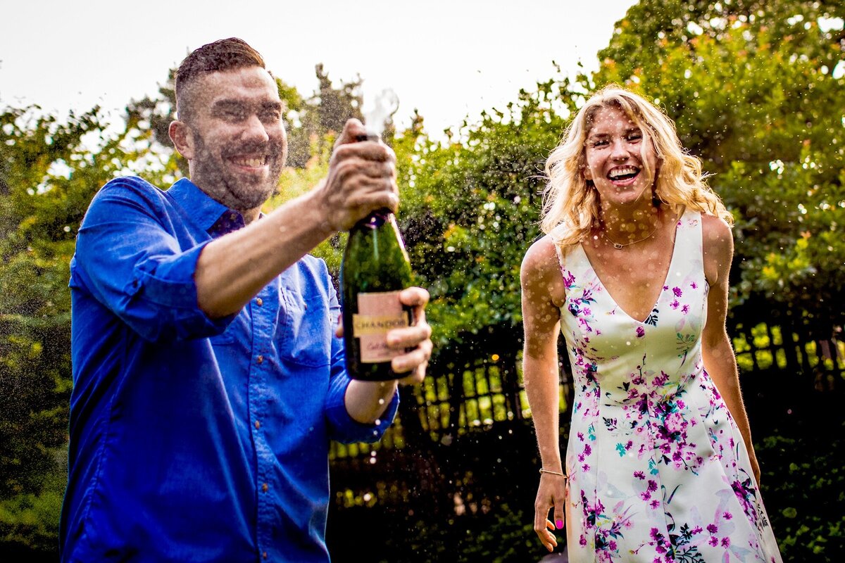 A couple sprays a bottle of champagne during a Garden of the Phoenix engagement session.