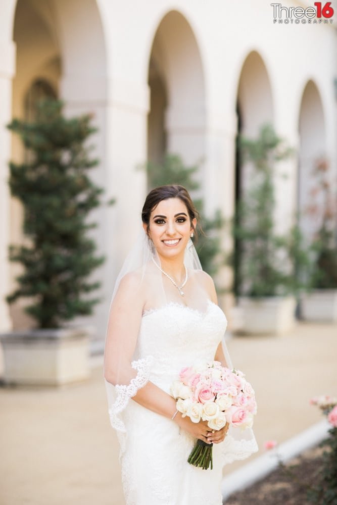 Bride poses with a large smile while holding her bouquet of flowers