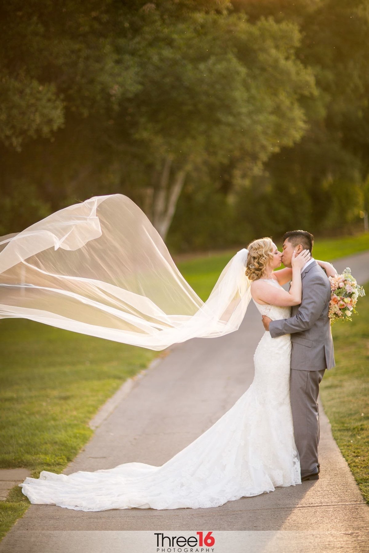 Bride and Groom share a passionate kiss on the golf course while the Bride's veil flies in the wind