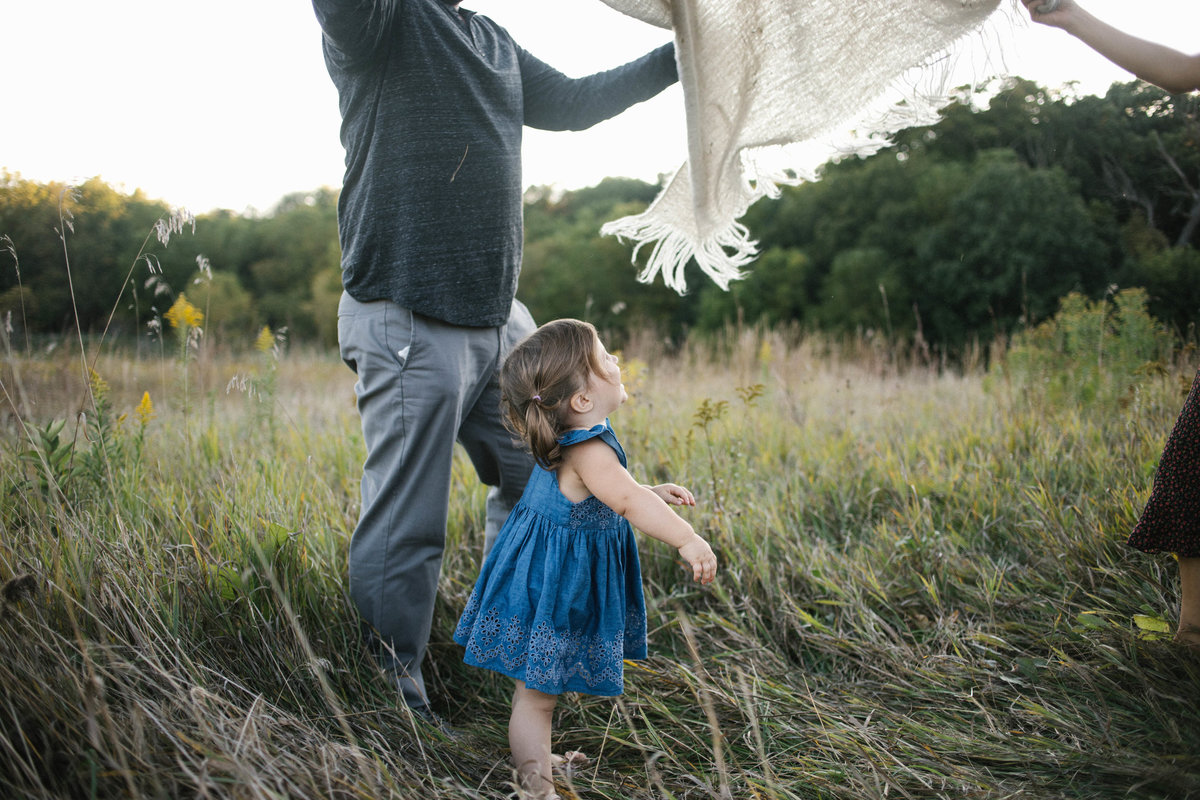 Parents playing peek a boo with little girl in a field