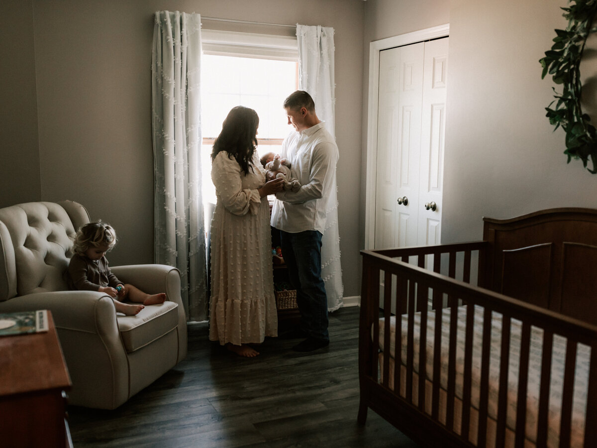 mom and dad holding newborn baby boy in nursery for in home lifestyle session