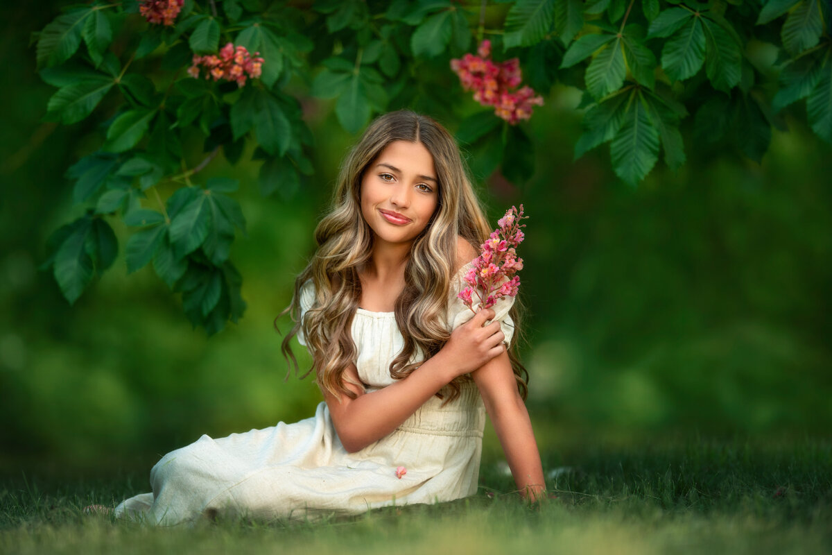 Teen girl sitting under a blooming pink chestnut tree on the grass