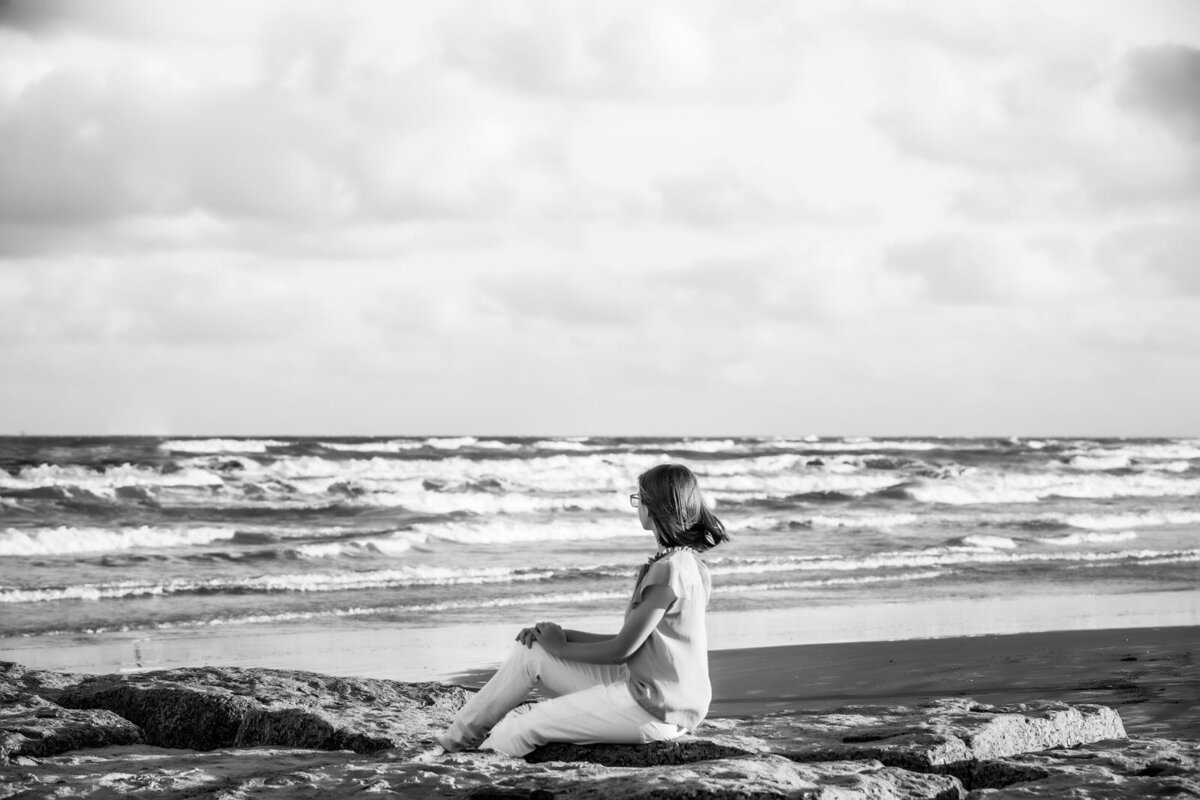 black-and-white-photograph-of-girl-sitting-on-rock-at-beach