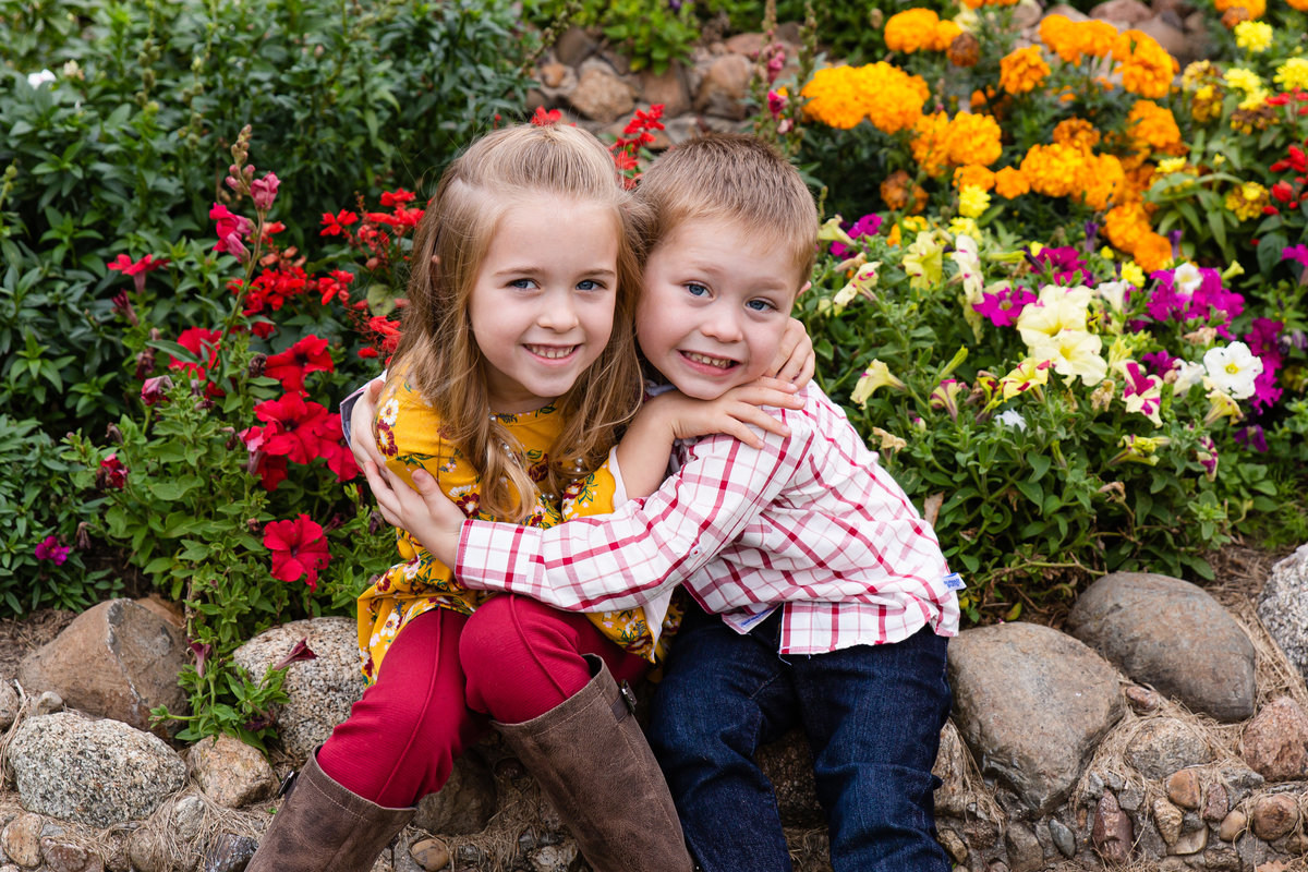 Siblings hug by beautiful Fall flowers during family photo session