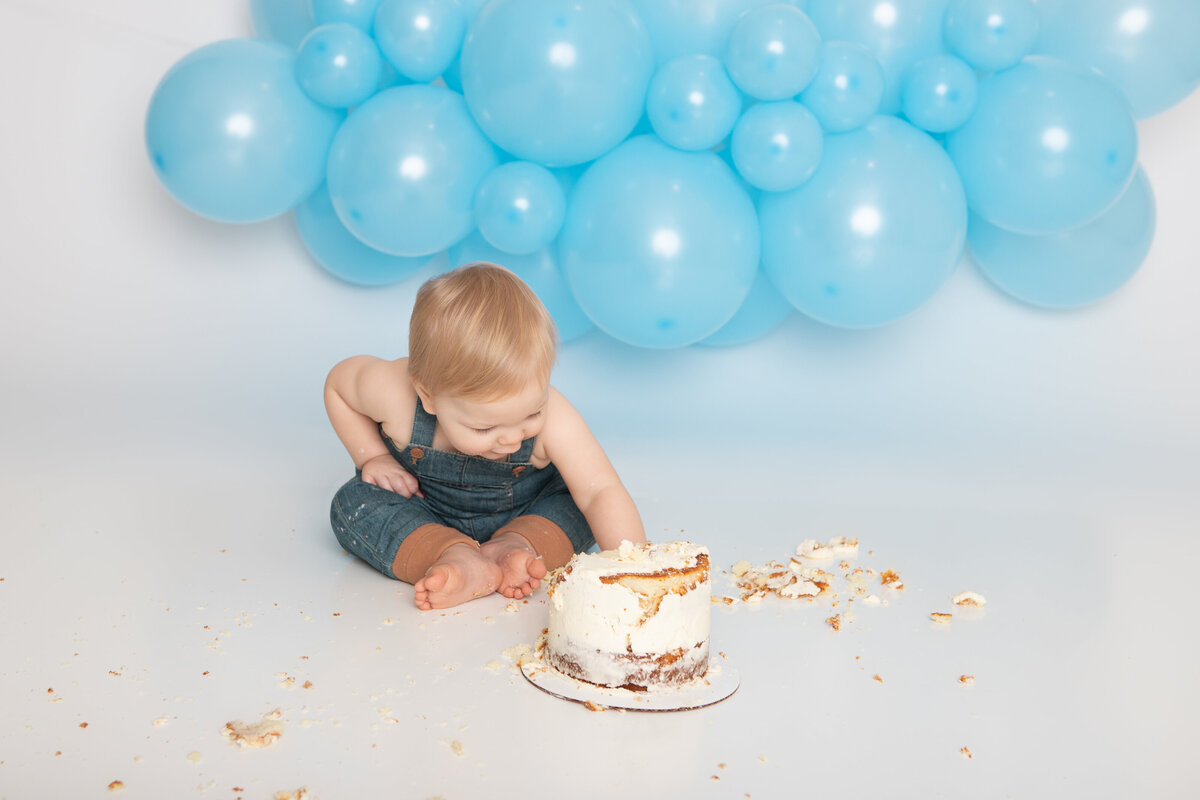 Baby eating a messy white cake with a blue balloon garland