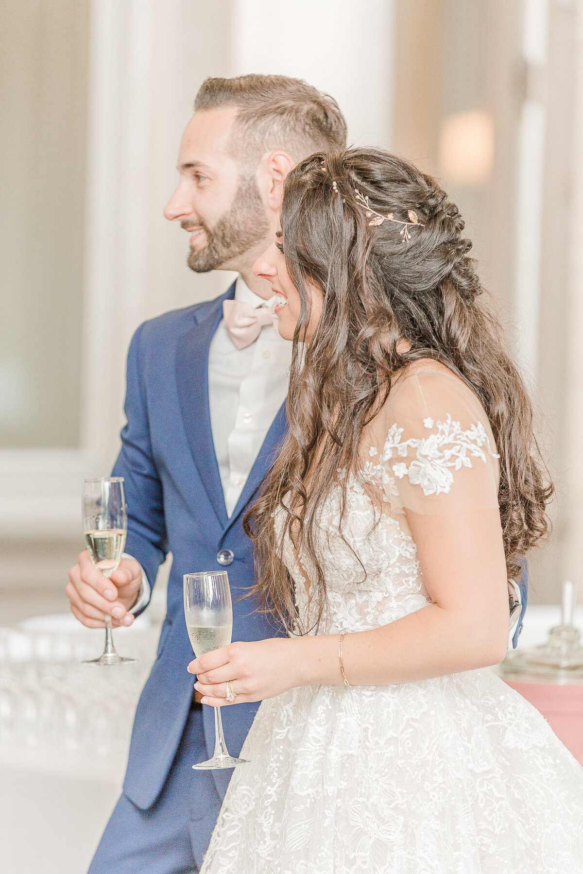 Bride and groom stand holding glasses of champagne at their Eolia Mansion wedding reception in Waterford, CT. Side profile close-up image. Bride and groom smiling as they are hearing speeches. Captured by best CT wedding photographer Lia Rose Weddings