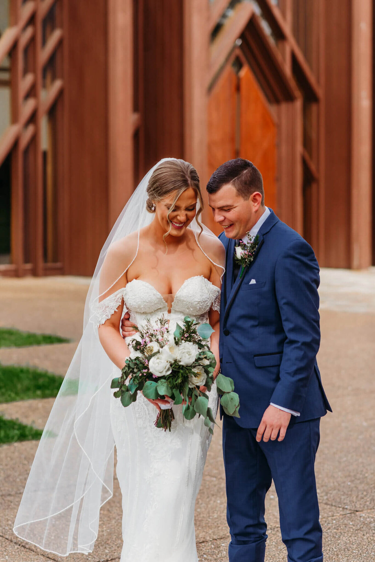 Photo of a bride and groom laughing while standing side-by-side in front of a wooden wedding chapel