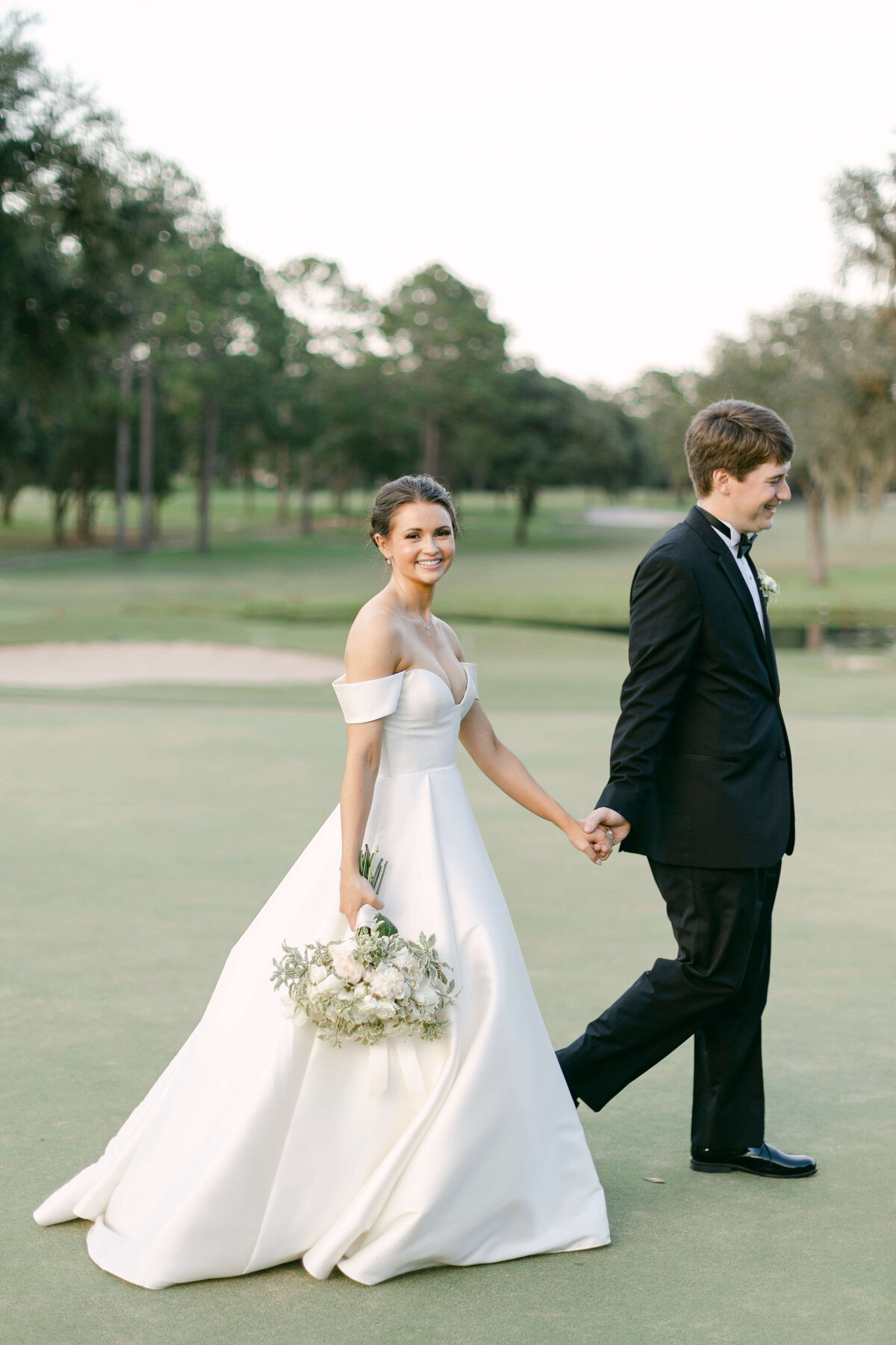 A bride and groom walk along a golf course.